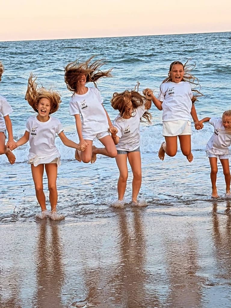 Studio dancers in team T-shirts jumping together at the beach