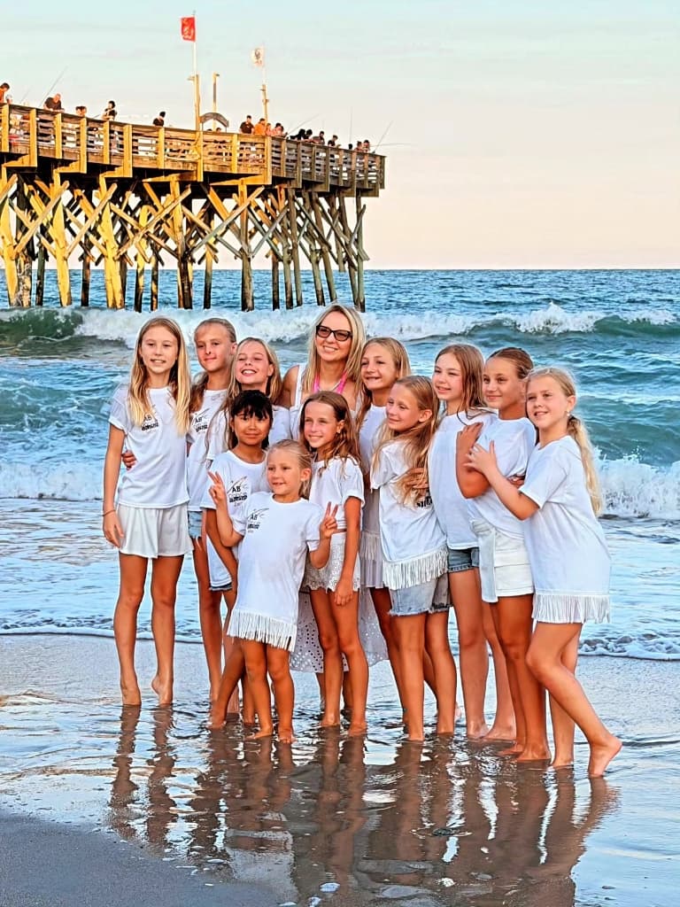 Studio dancers and their teacher posing together on the beach at sunset