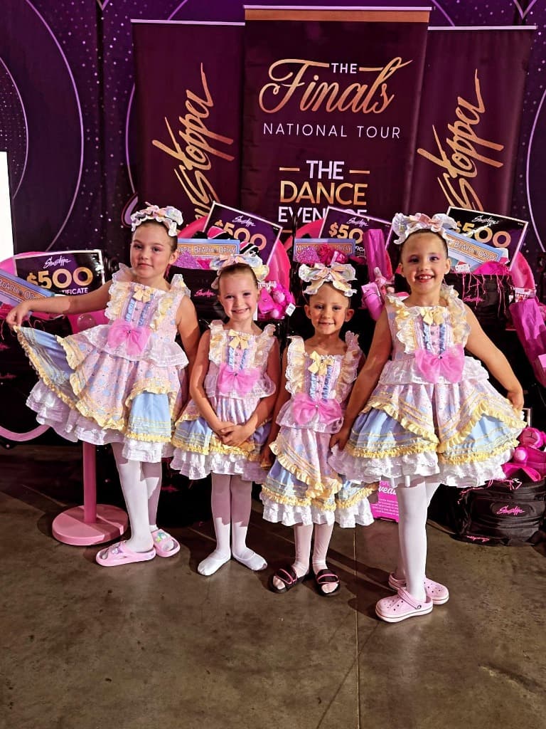 Four smiling young dancers in pastel costumes at The Finals national tour